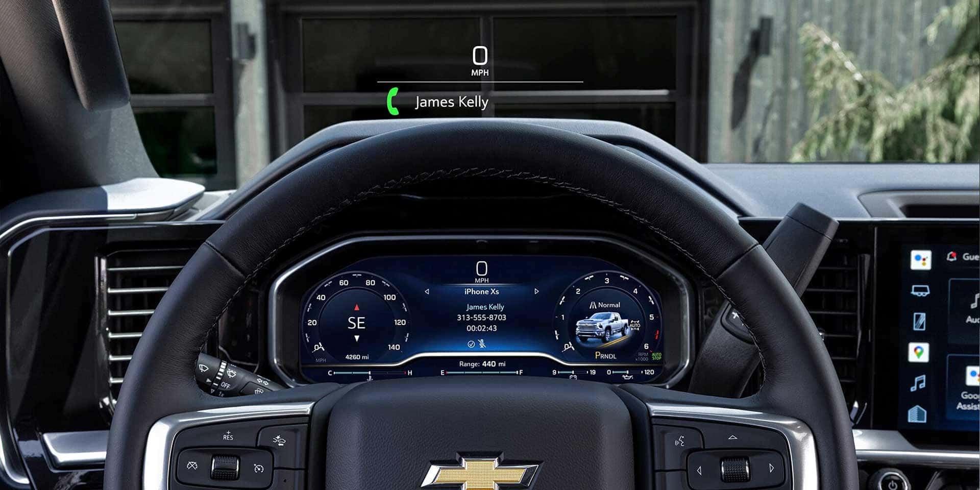 View of a car steering wheel with a digital dashboard showing speed and navigation. A virtual display indicates an incoming call from James Kelly. The Chevrolet logo is visible on the steering wheel.