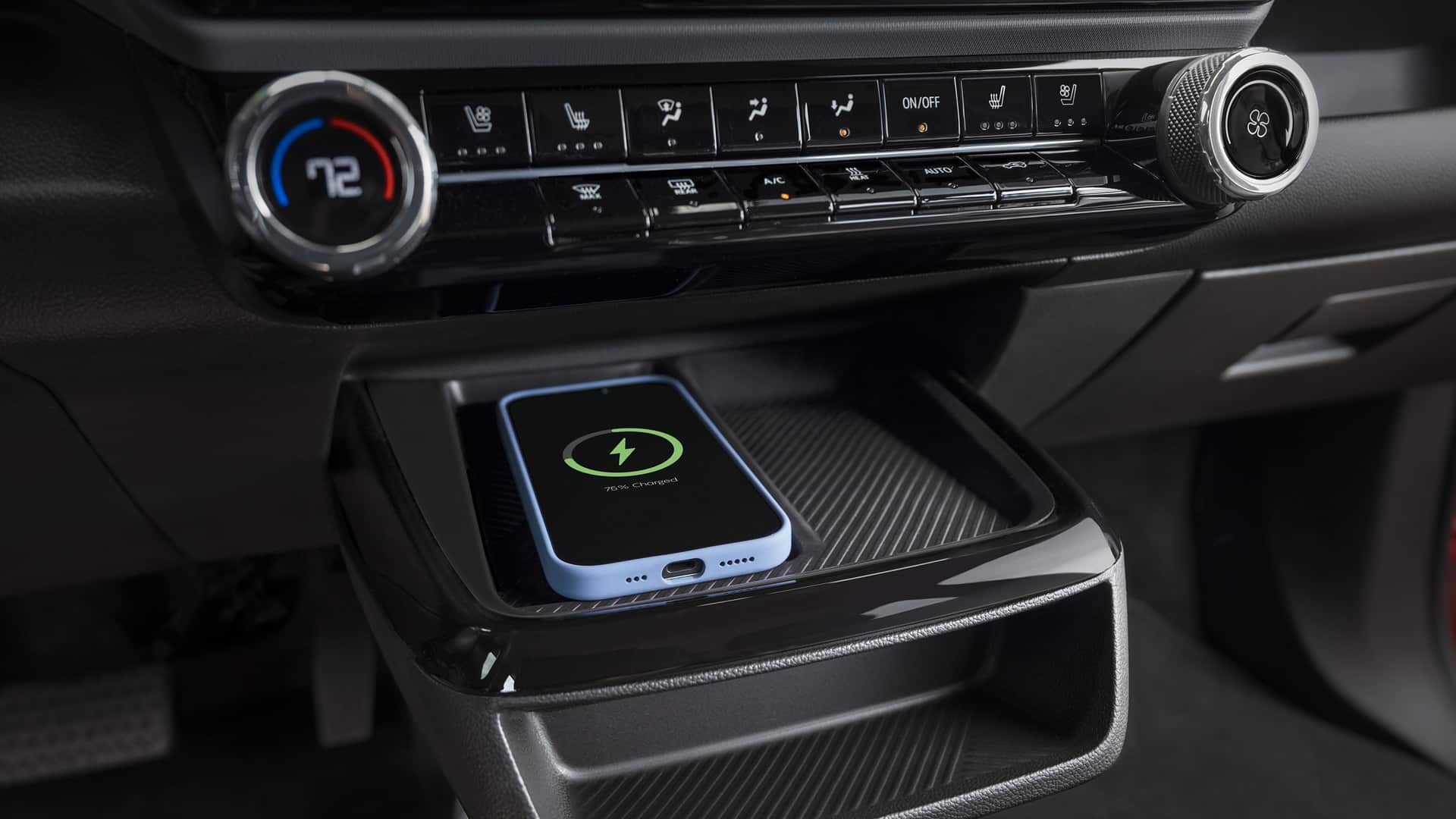 Smartphone wirelessly charging in a car's console, alongside climate control buttons.
