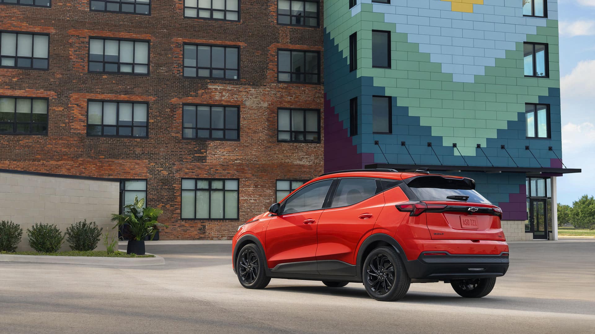 A gray Chevrolet SUV is driving on a two-lane road with yellow lines. The background shows blurred greenery, indicating motion. The SUV has a sleek design with distinctive front grille and headlights.