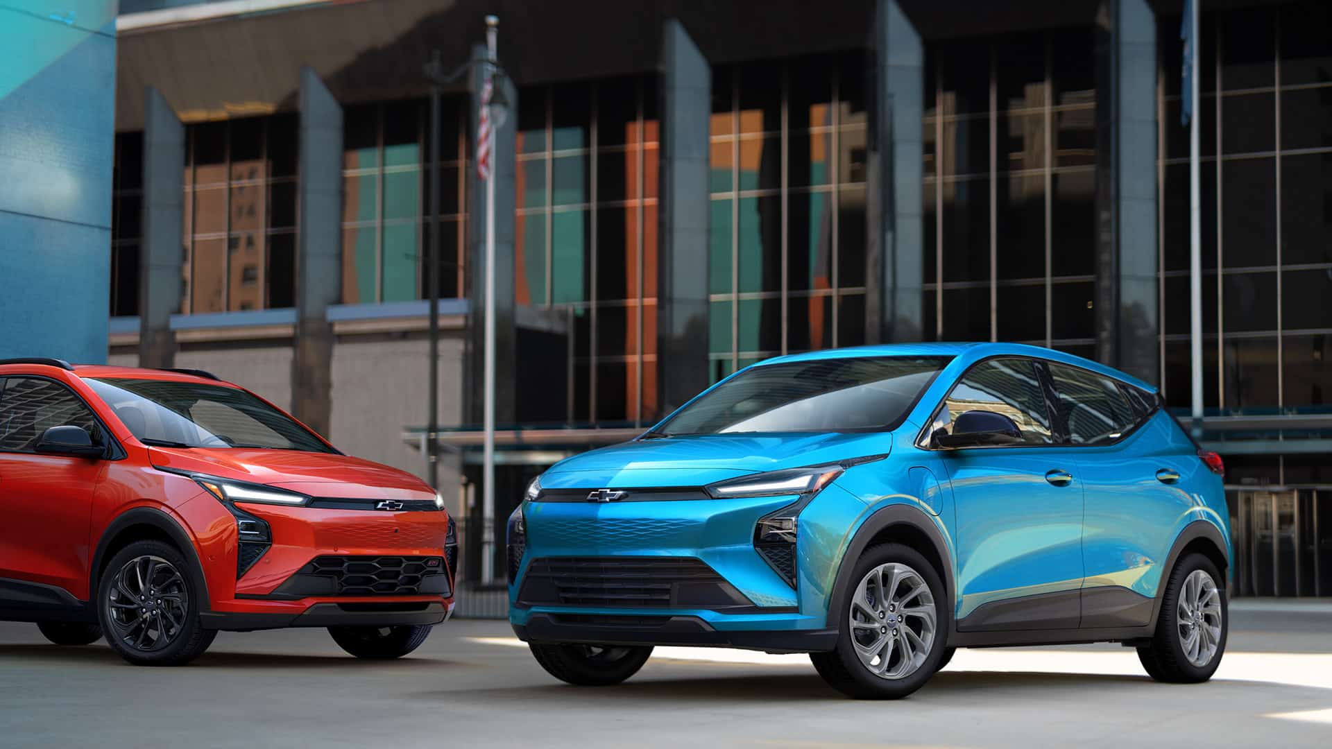 Two Chevrolet electric SUVs, one blue and one red, parked in front of an urban building.