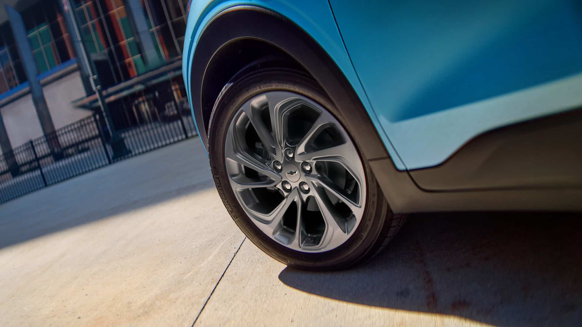 Close-up of a car's alloy wheel and tire on a blue vehicle, parked on a concrete surface.
