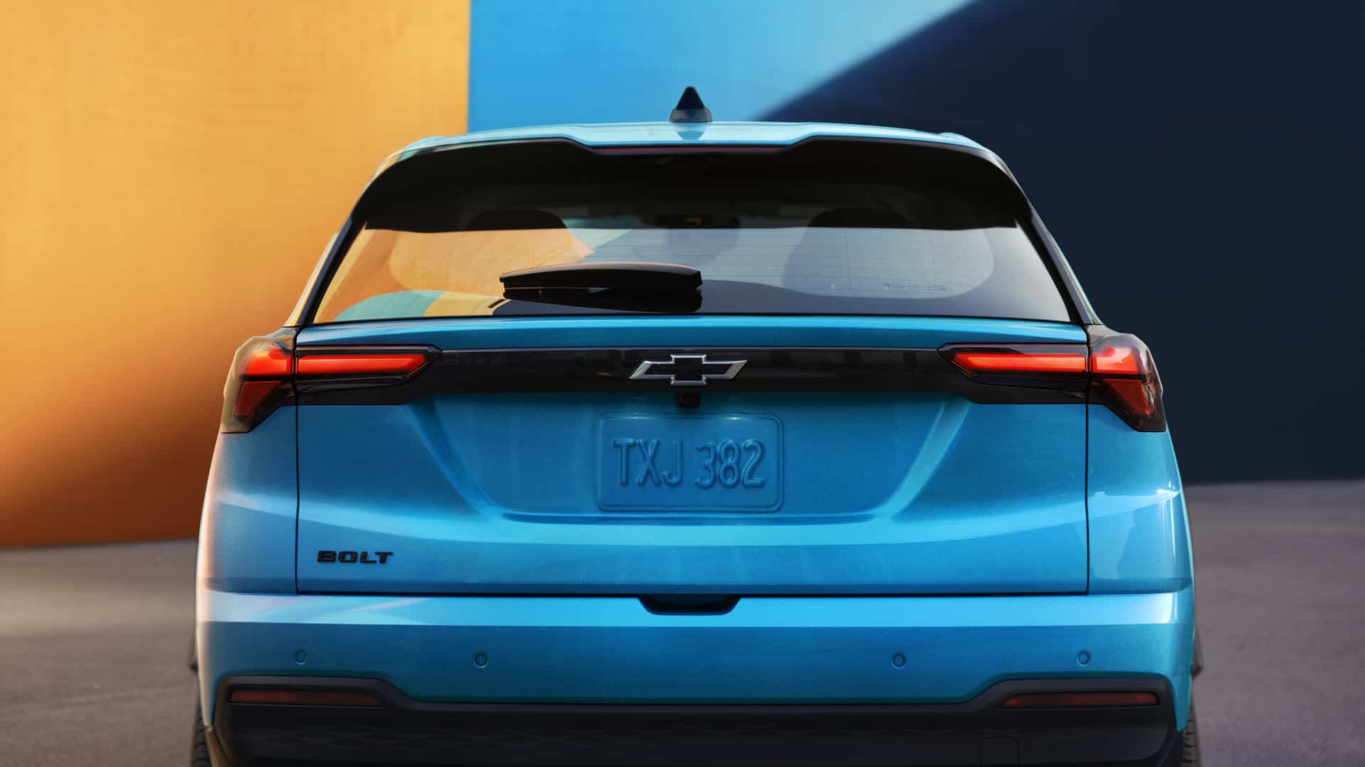 Rear view of a blue Chevrolet Bolt electric vehicle against a vibrant orange and blue background.