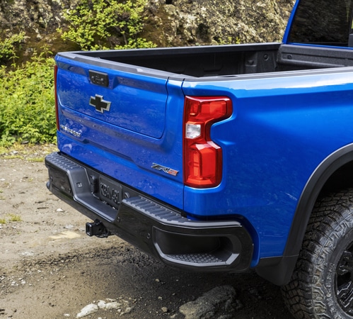Blue pickup truck rear view, parked on rocky terrain, showcasing the open truck bed and tailgate.