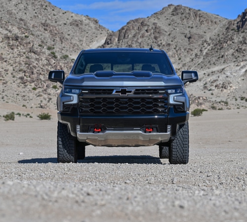 A black pickup truck on a rocky desert landscape with mountains under a clear blue sky.