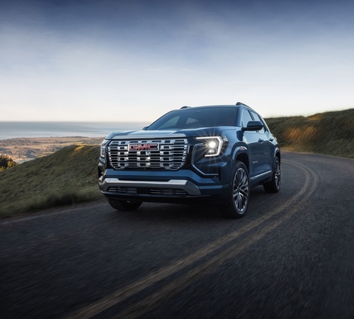 Blue SUV driving on a scenic coastal road with grassy hills and ocean views.