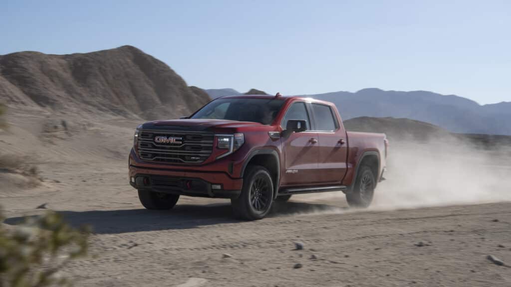 Red GMC pickup truck driving through a desert landscape, kicking up dust.