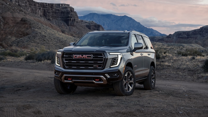 GMC SUV parked in a rugged desert landscape with rocky hills at dusk.