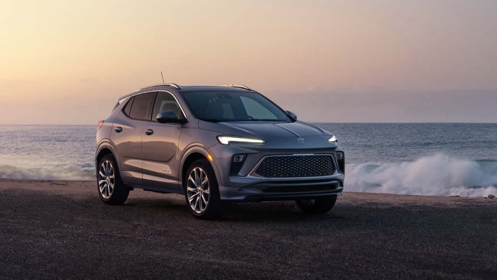 A silver SUV parked by the ocean at sunset, waves crashing gently in the background.