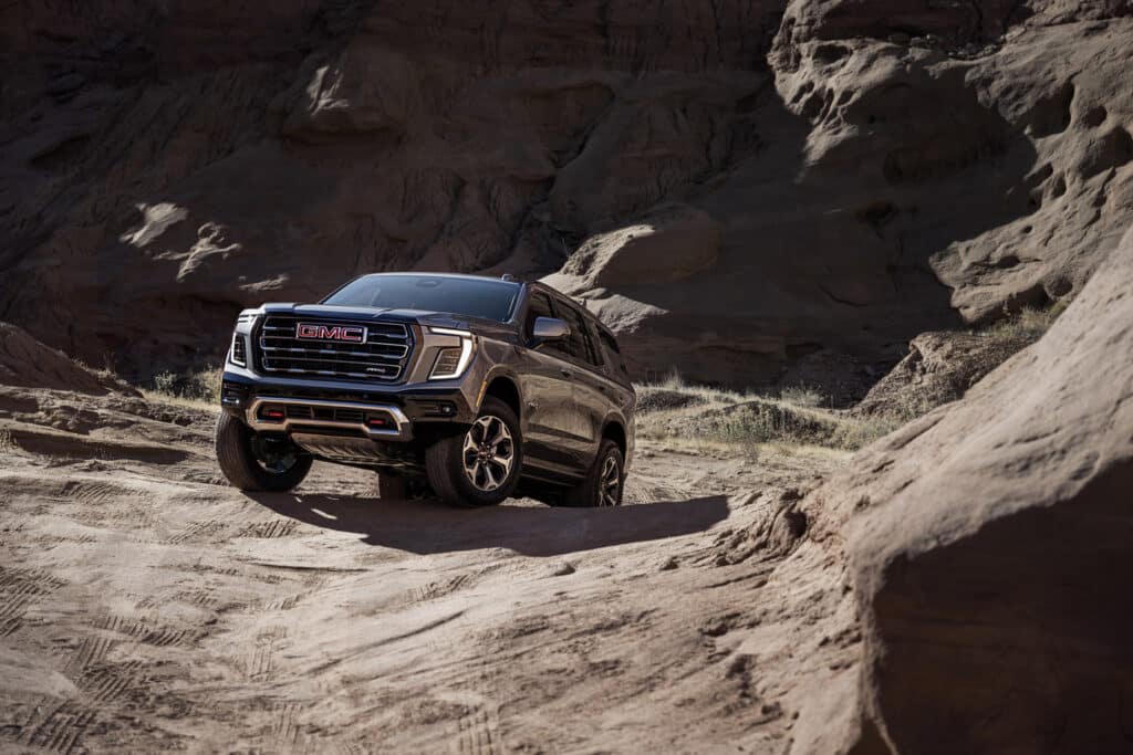 A black GMC SUV drives off-road through a rugged desert landscape, showcasing its rugged capability.
