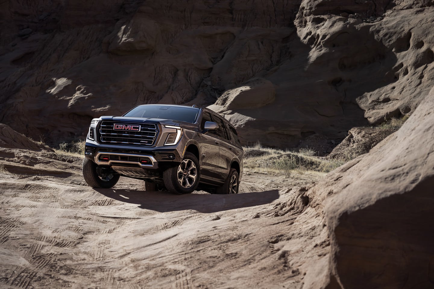 A black GMC SUV drives off-road through a rugged desert landscape, showcasing its rugged capability.