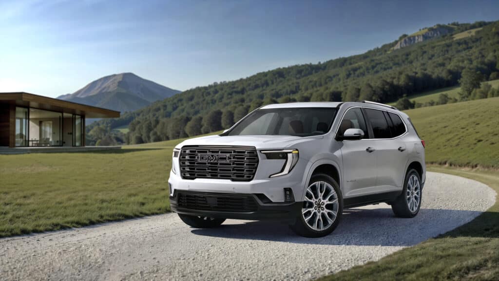 Silver GMC SUV parked on a rural road with mountain and modern house in the background.