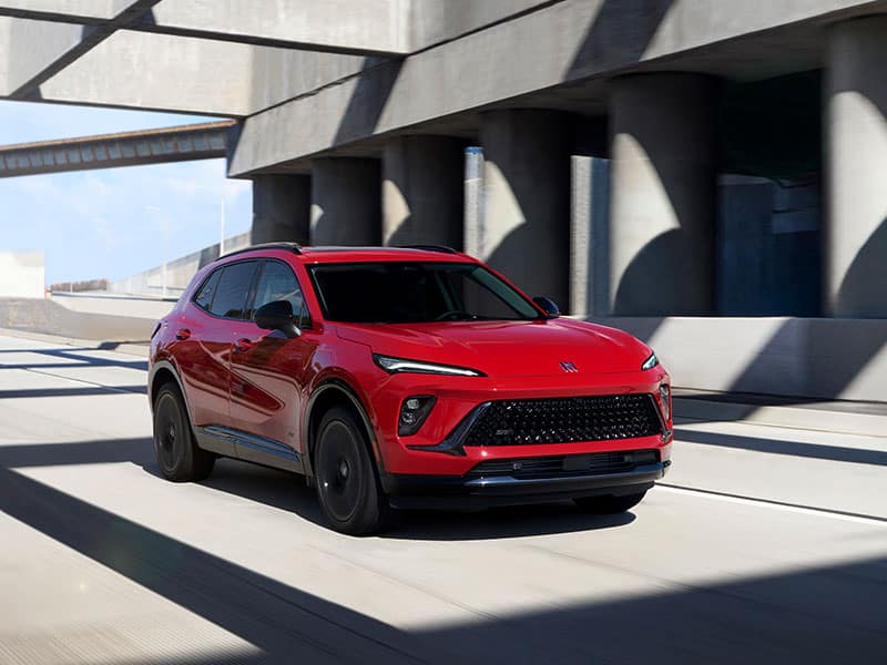 Red SUV driving on a concrete overpass with clear blue skies in the background.
