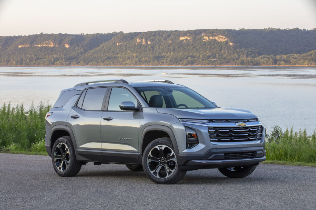 Silver SUV parked by a lake with a scenic, tree-lined backdrop under a clear sky.