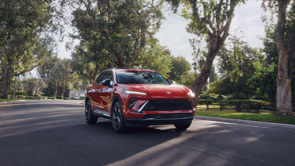 Red SUV driving on a scenic tree-lined road, showcasing its sleek design and dynamic performance.