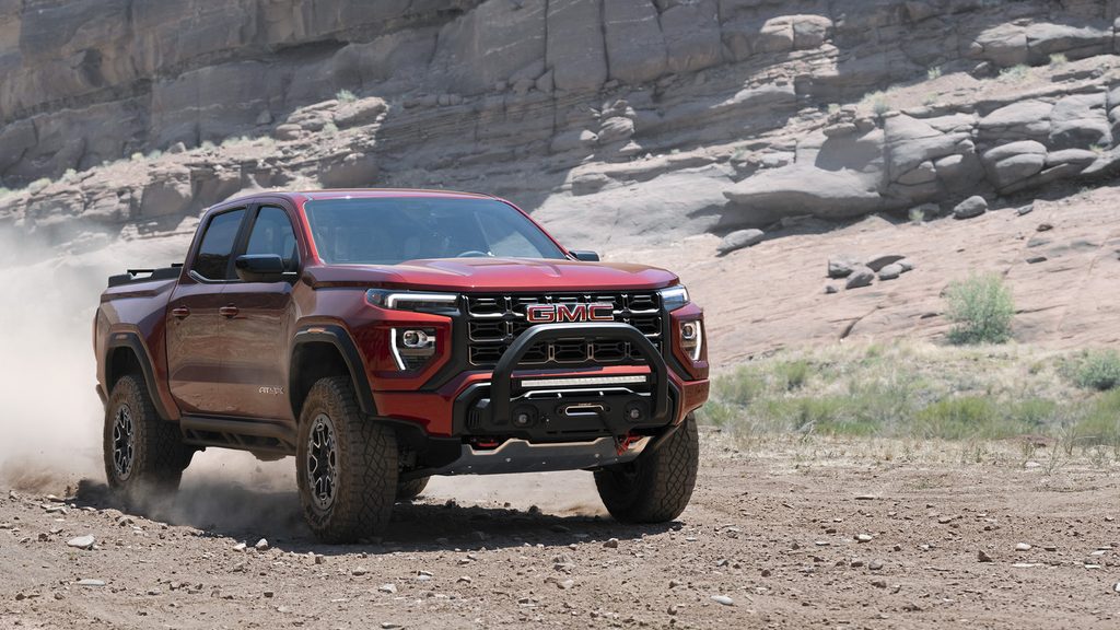 Red GMC truck driving off-road through rocky desert terrain.