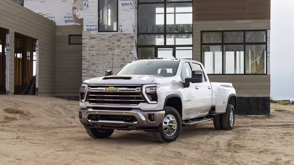 White pickup truck parked on dirt in front of a modern house under construction.