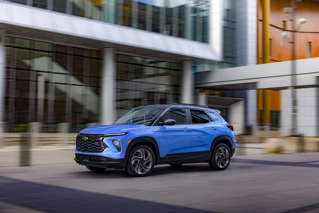 Blue SUV driving past modern glass building, showcasing sleek urban design.
