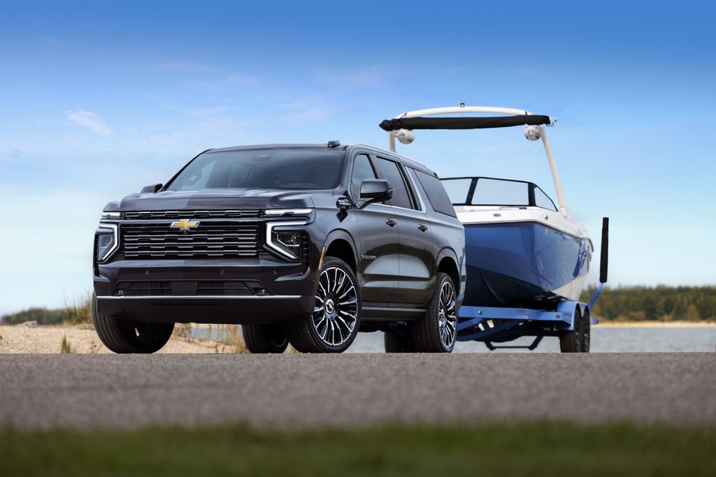 SUV towing a blue boat on a trailer by a lake, under a clear blue sky.