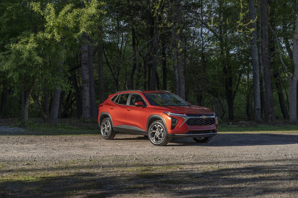 Red Chevy SUV parked on a dirt path in a wooded area, under dappled sunlight.